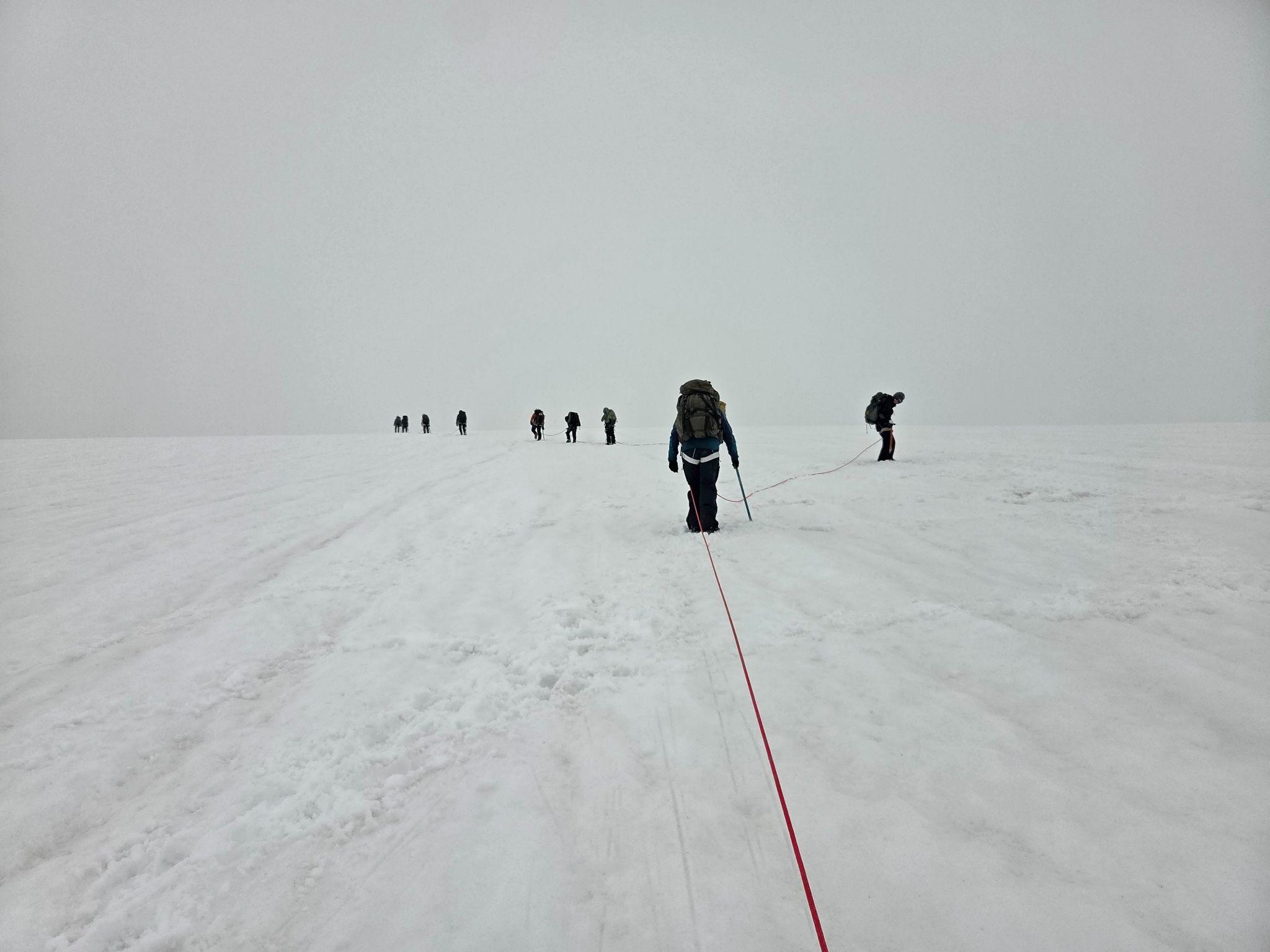 Climbers connected by rope moving across the Easton Glacier in fog